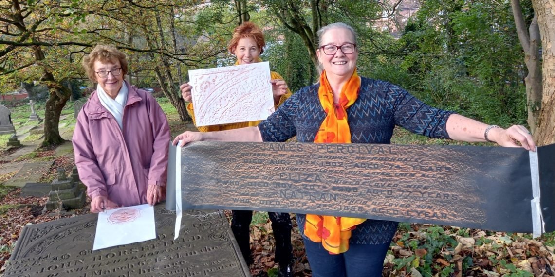 Three workshop participants holding up their finished rubbings beside the gravestones at St Mary’s Churchyard