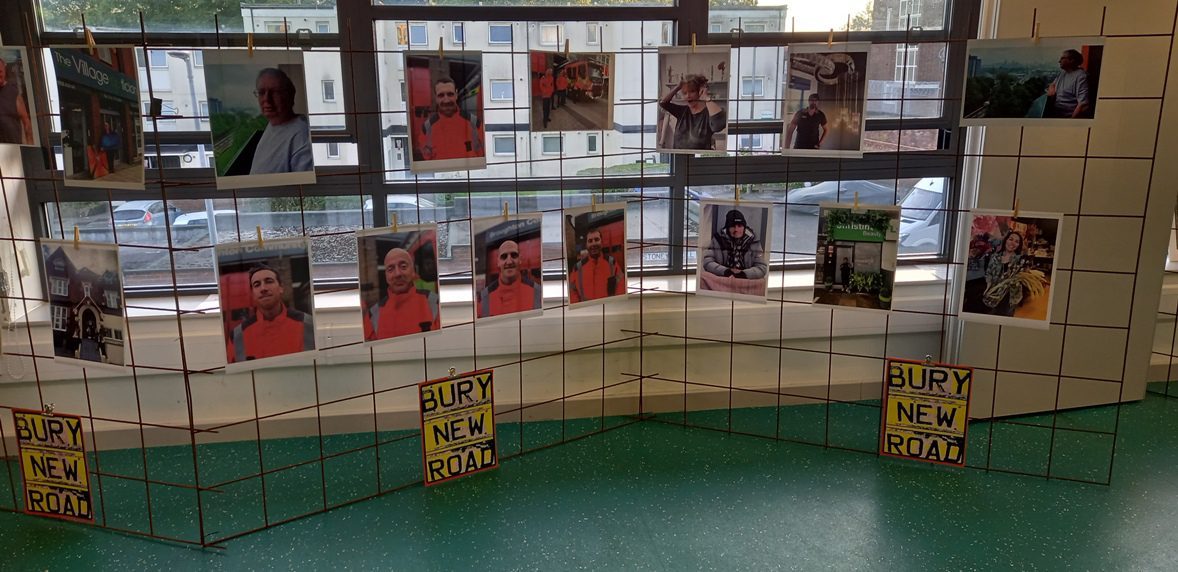 Wall display of portrait photographs, including local firefighters, from the Bury New Road exhibition