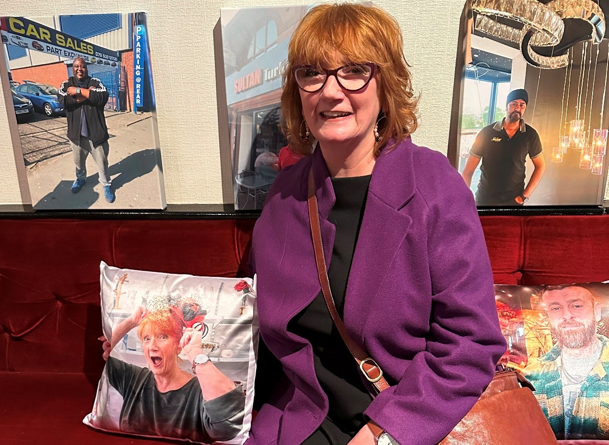 Louise Garman seated with three canvas portraits from the Portraits Exhibition and a cushion printed with a portrait