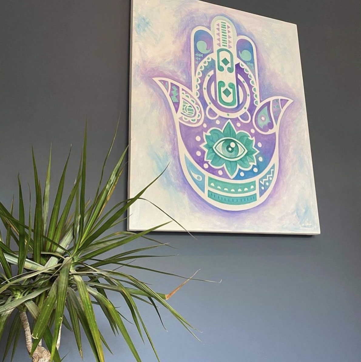 Hamsa hand painting with an eye and lotus motif, in purple, teal and white