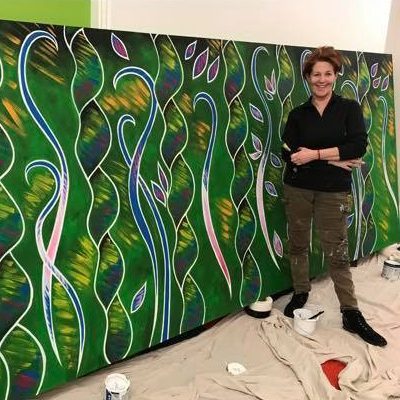 Louise Garman with a large green canvas painted with abstract vines and leaves