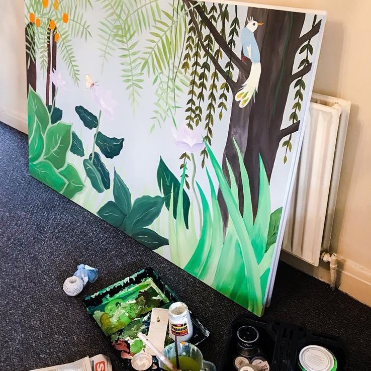 Canvas painted with jungle foliage and a bird in the branches, resting against a wall