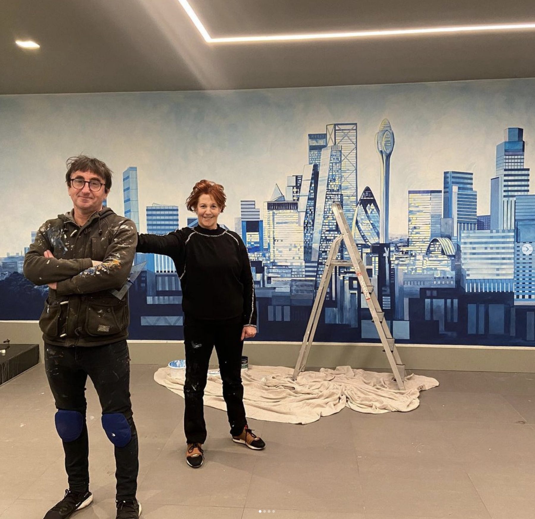 Louise Garman and an assistant standing beside the completed London skyline mural