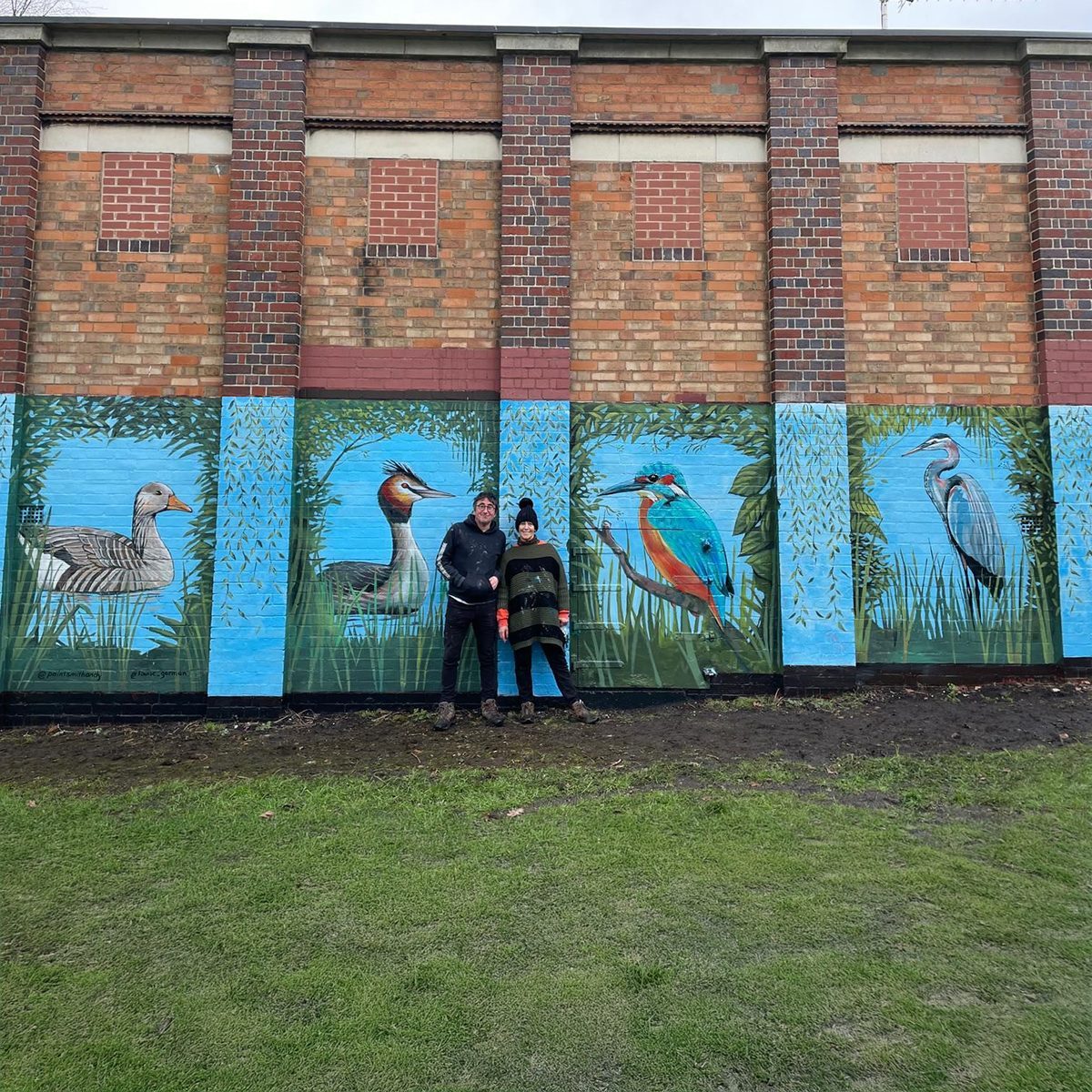 Wildlife mural featuring a duck, grebe, kingfisher and heron on the Trittiford Park building, with the artists standing in front