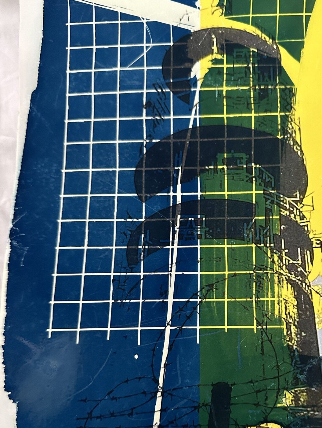 Detail of a mixed-media work with wire grid, barbed wire and layered blue, green and yellow print