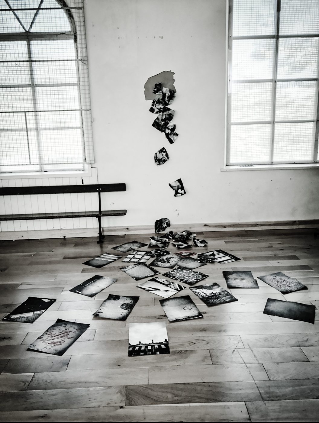 Torn paper fragments arranged in an exclamation-mark shape on the wall, cascading to a spread of textured prints on the floor, at Church, New Mills Arts Festival