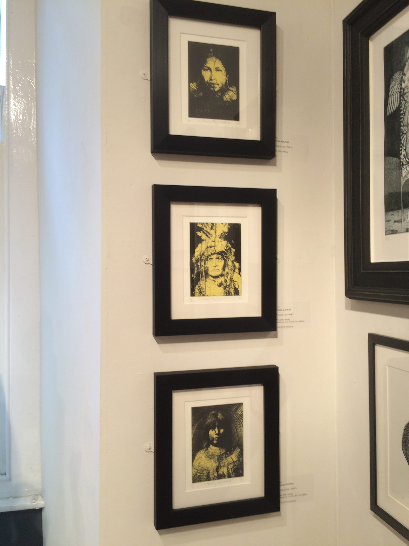 Three framed yellow and black portrait prints mounted on a white gallery wall, at Mall Galleries, London