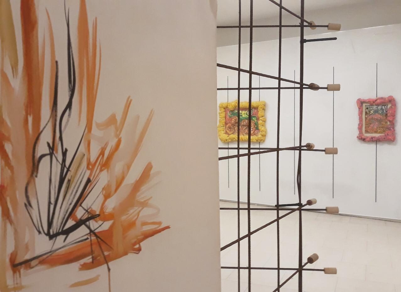 An orange and black ink wall piece beside a floor-standing wire grid frame holding two small framed collages, at New Shift, Castlefield Gallery