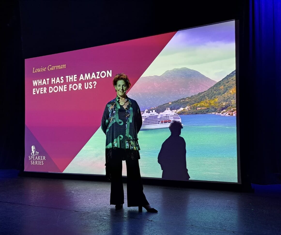 Title slide reading WHAT HAS THE AMAZON EVER DONE FOR US? with Louise Garman standing beside it aboard the Regent Seven Seas Mariner
