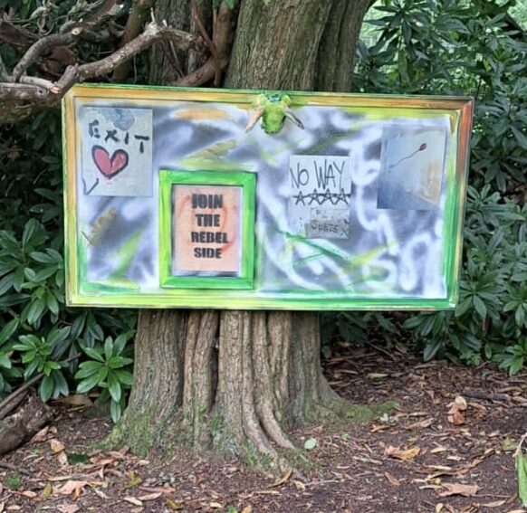 A painted board reading EXIT, JOIN THE REBEL SIDE and NO WAY, mounted against a tree at the Big Heart Little Hulton event