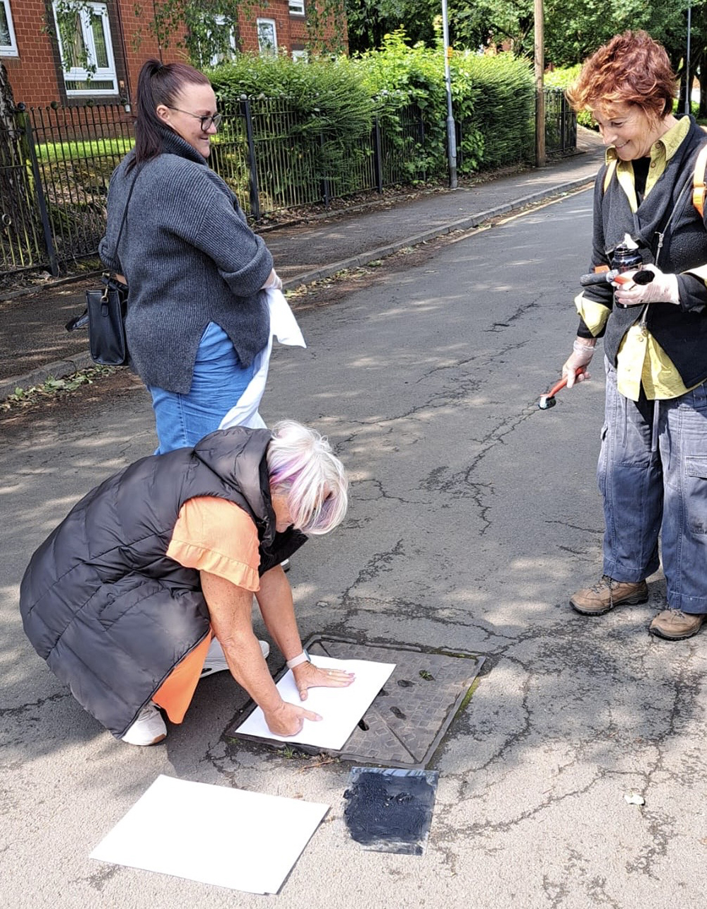 Louise Garman and volunteers taking a print from a drain cover on a Bolton street
