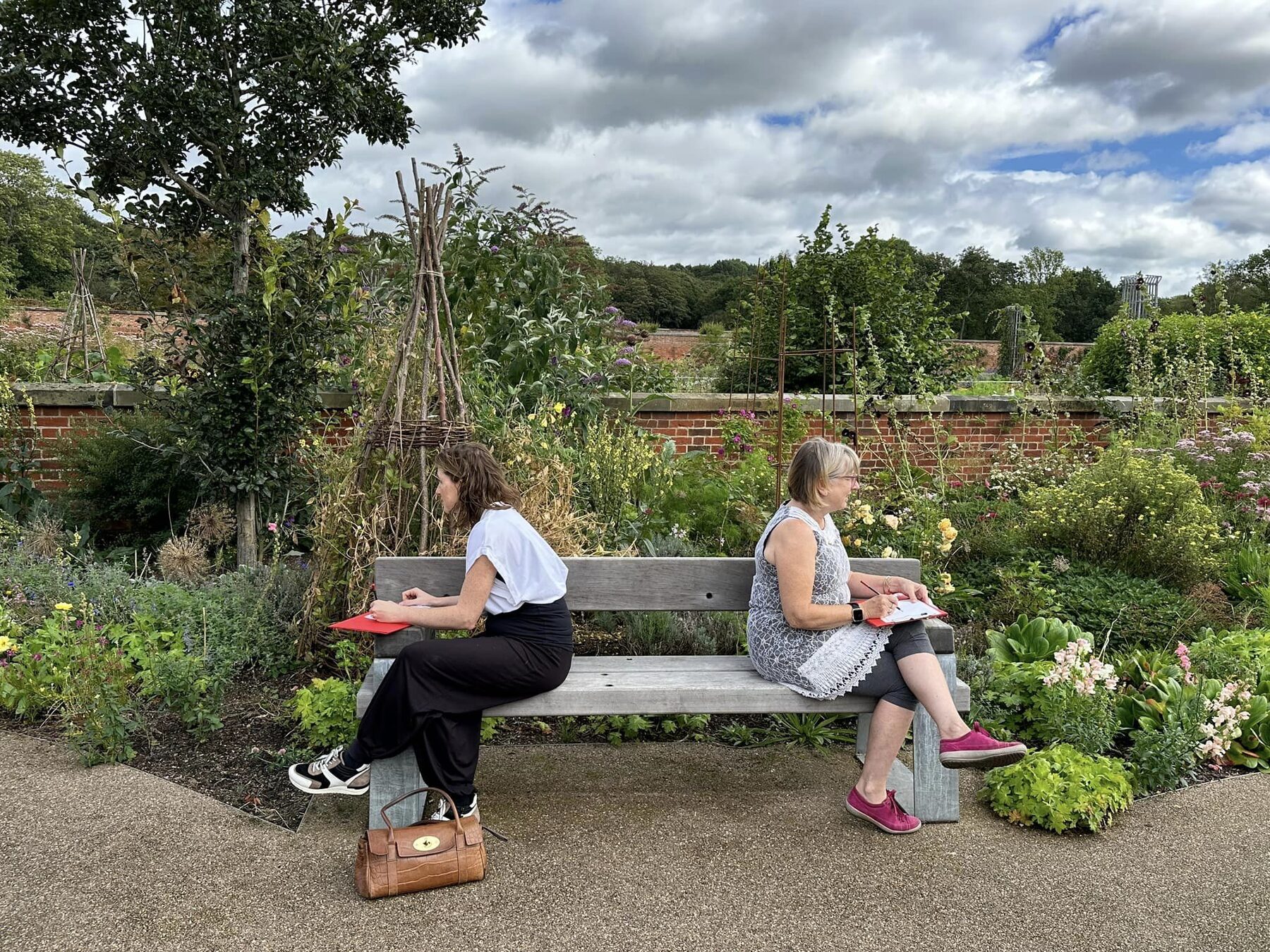 Two workshop participants sketching on a bench in the walled garden at RHS Garden Bridgewater