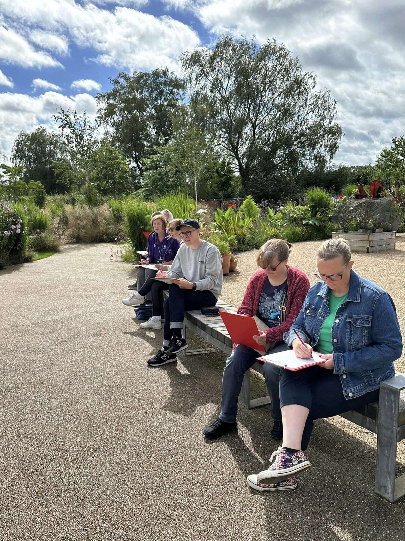 A group of workshop participants sketching outdoors on clipboards in the sunshine