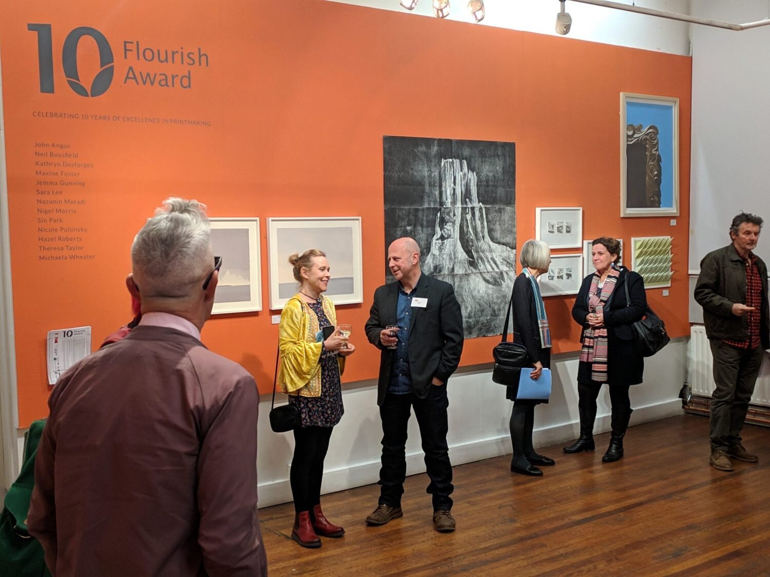Visitors viewing framed prints on the orange 10 Flourish Award exhibition wall