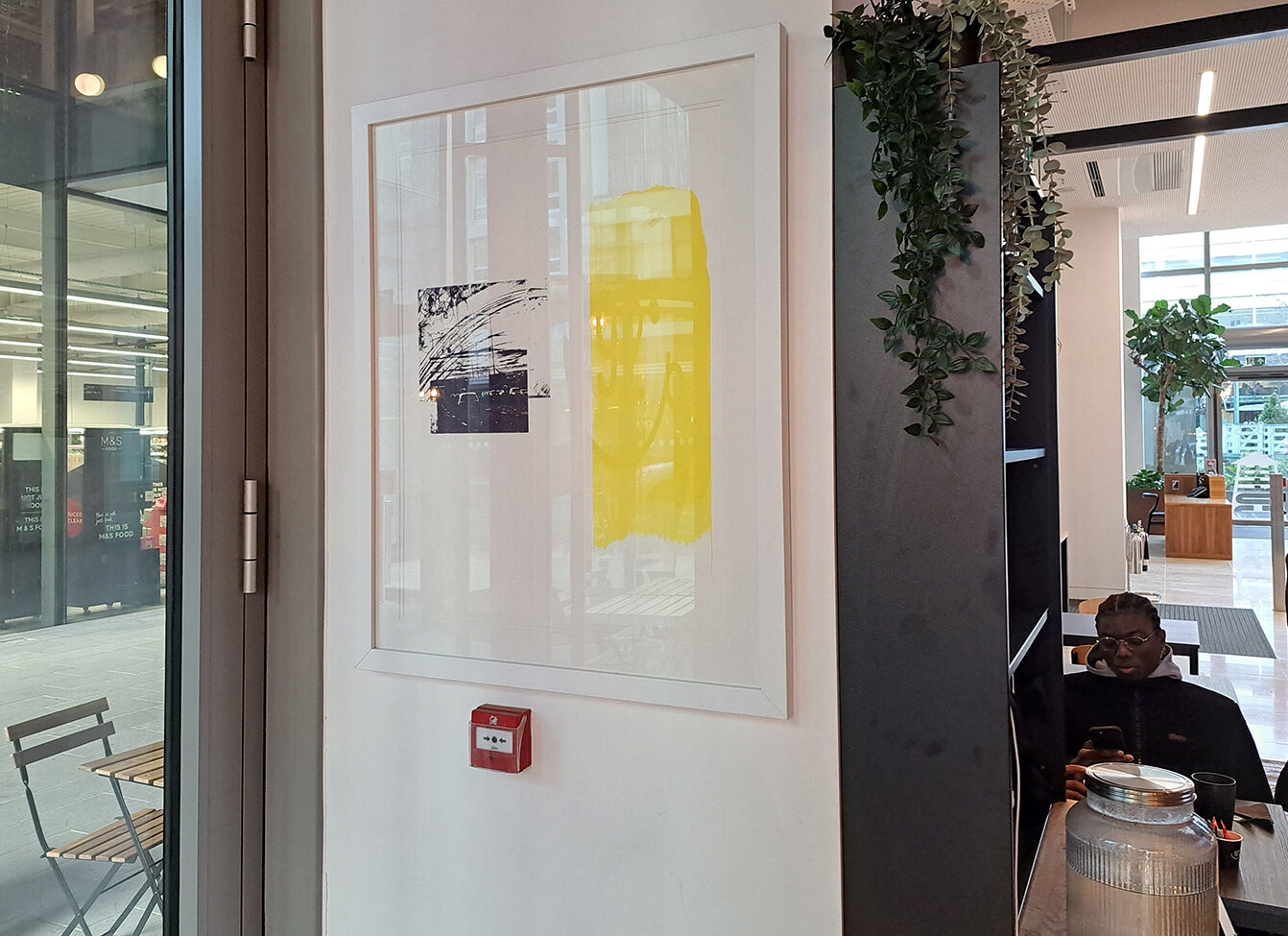 A framed print with black linework and a yellow wash, hanging at 92 Degrees Coffee