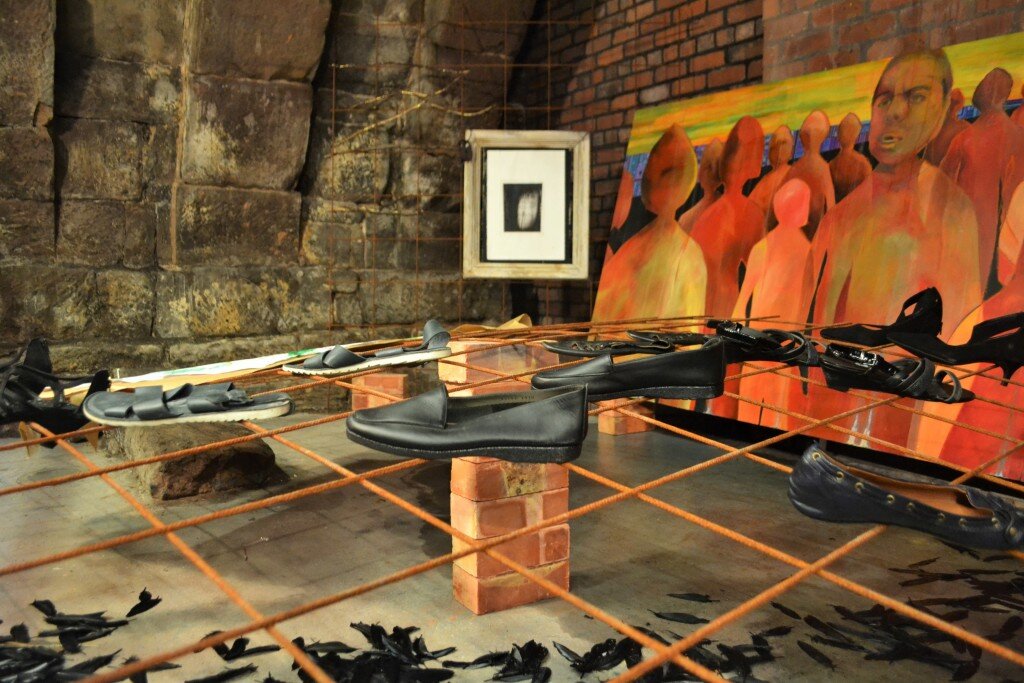 Louise Garman's To Walk In Beauty installation under Hanging Bridge, with shoes on brick pedestals inside a rusted metal grid, a painted figures canvas and a small framed photograph