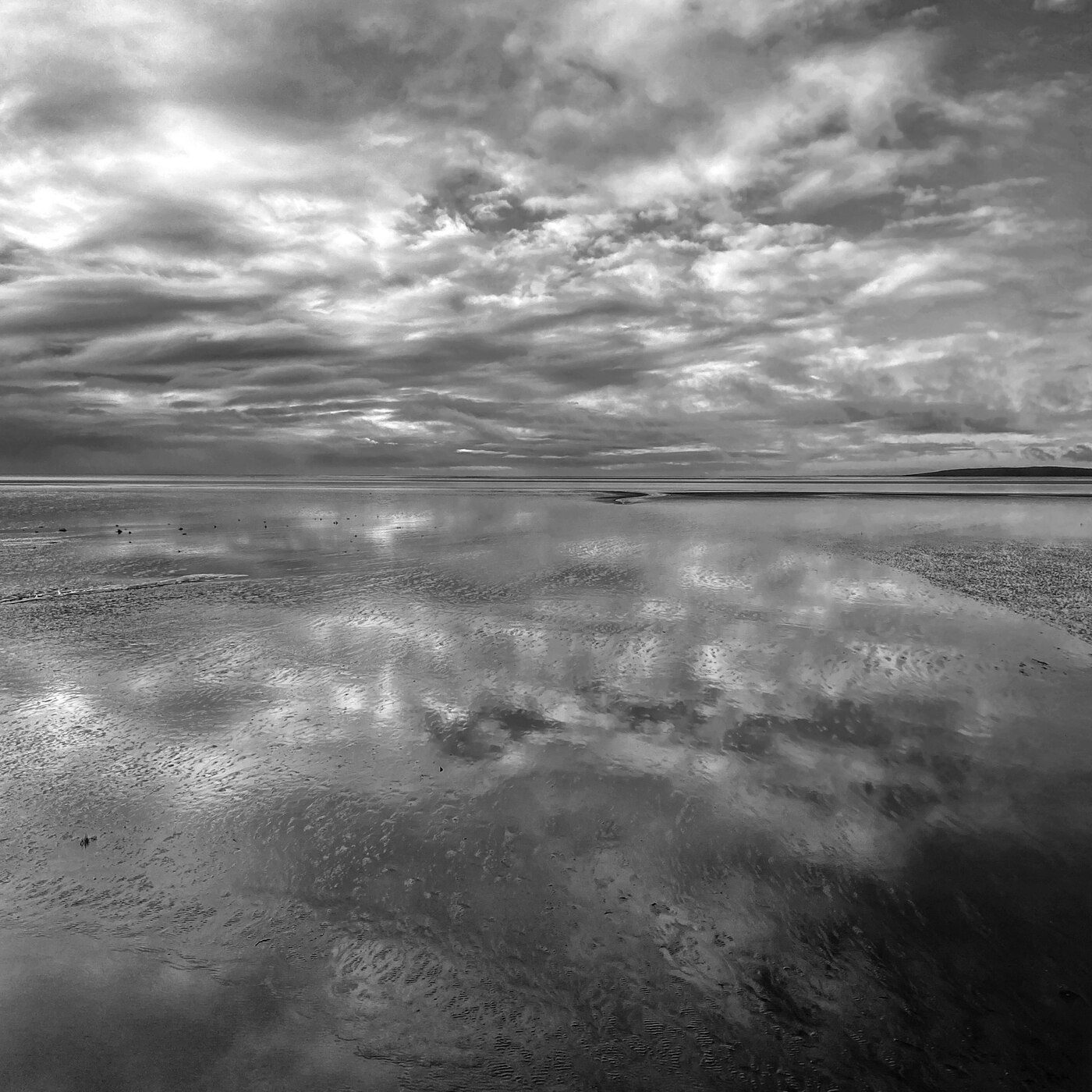 Black and white photograph of a tidal flat with reflected clouds