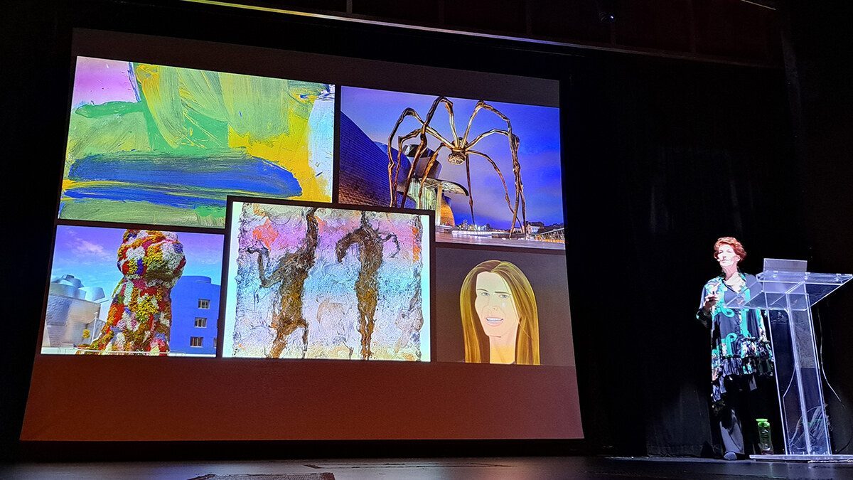 Louise Garman delivering an art talk on stage, screen showing Guggenheim Bilbao artworks