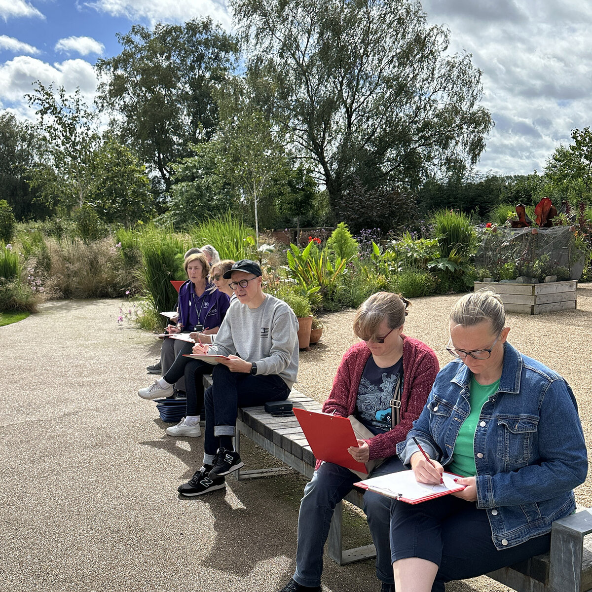 Workshop participants sketching on clipboards on a bench outdoors