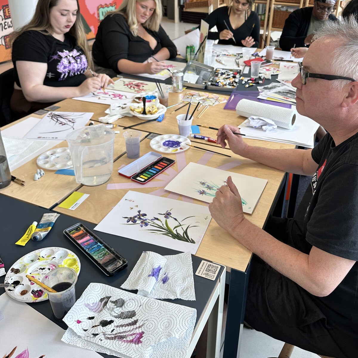 Workshop participants painting watercolour irises and floral studies around a table